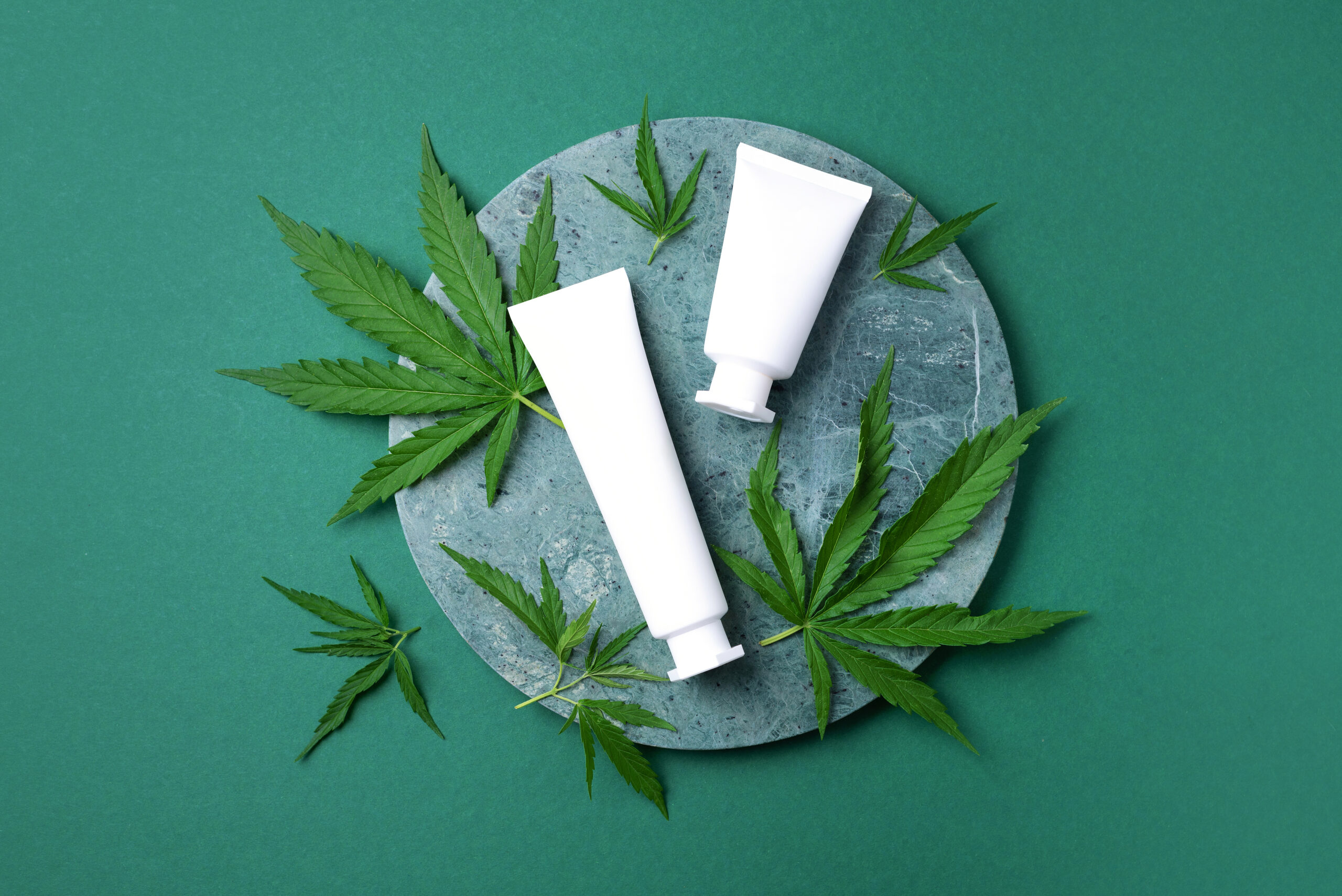 Cosmetic product with CBD oil and hemp leaves on marble background. Flat lay, copy space. Top view. Natural skin care. Cream with hemp oil and marijuana leaves