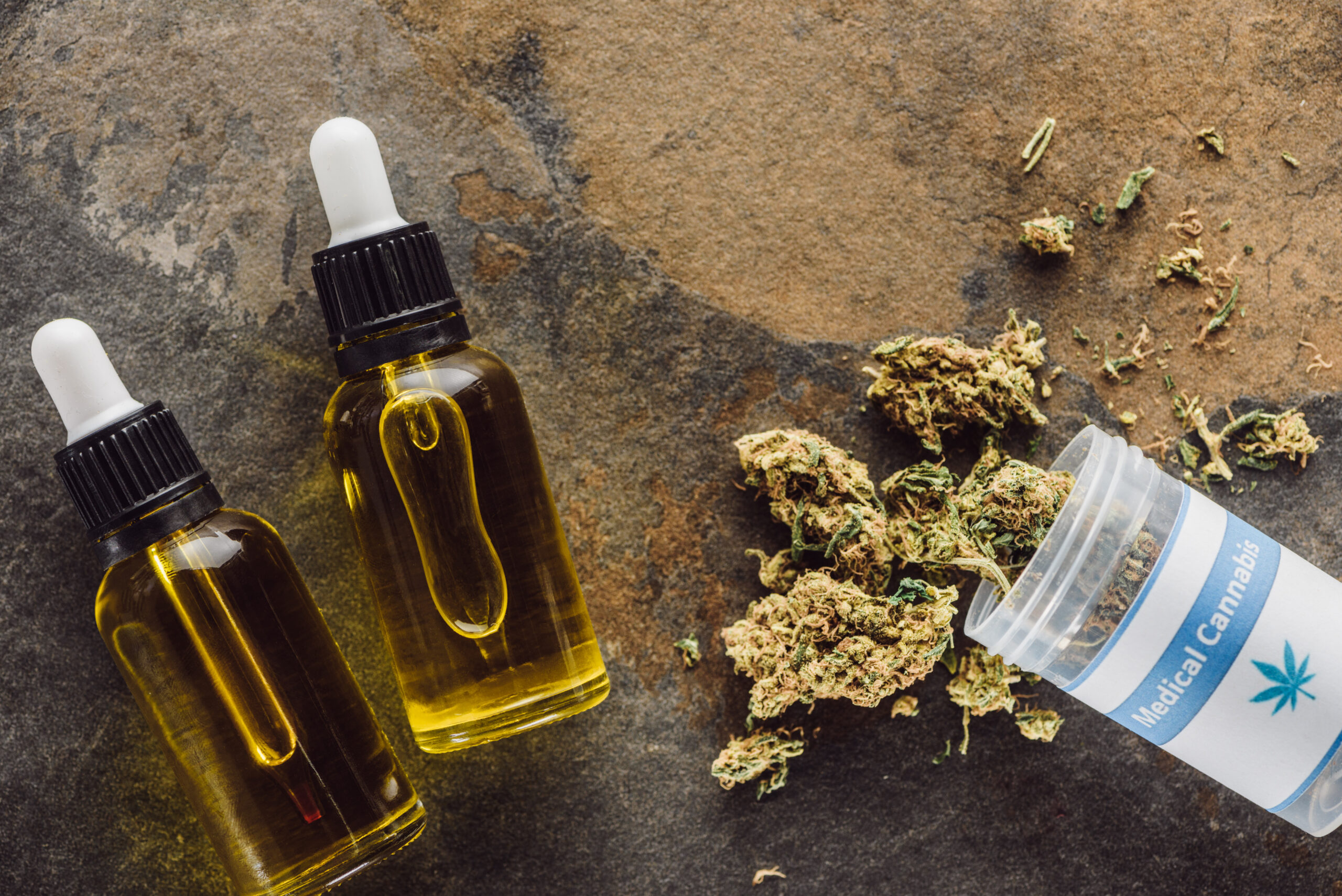 Top View of Medical Marijuana Buds Near Container And Bottles With Hemp Oil on Marble Surface